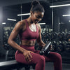 Woman in maroon workout outfit using a Rechargeable Massage Gun  in a gym setting
