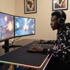 Person playing a video game on a dual monitor setup with a large desk pad.