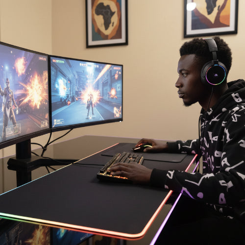 Person playing a video game on a dual monitor setup with a large desk pad.